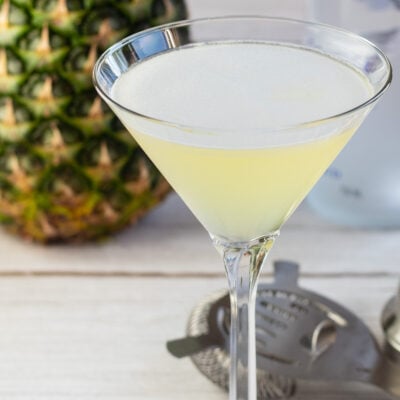 正方形的菠萝马提尼酒的图像，后面有新鲜的菠萝。